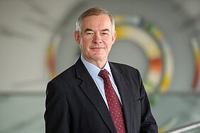 Porträt von Christoph Wanner mit dunklem Anzug und weinroter Krawatte im Flur des ZIM.
