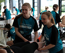 Beim Marathon massieren zwei Schülerinnen eine Läuferin.
