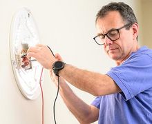 Für mehr Informationen hier klicken Ein Handwerker tauscht ein Leuchtmittel einer Wandlampe
