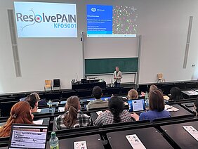 Prof. Dr. Niels Eijkelkamp im Hörsaal vor Gästen des Kick-Off-Meetings. An der Wand eine Powerpoint Präsentation und das Logo der Klinischen Forschungsgruppe KFO5001.