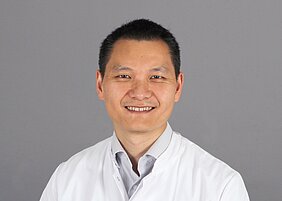 Porträtfoto von Chi Wang Ip im weißen Kittel vor grauem Hintergrund 