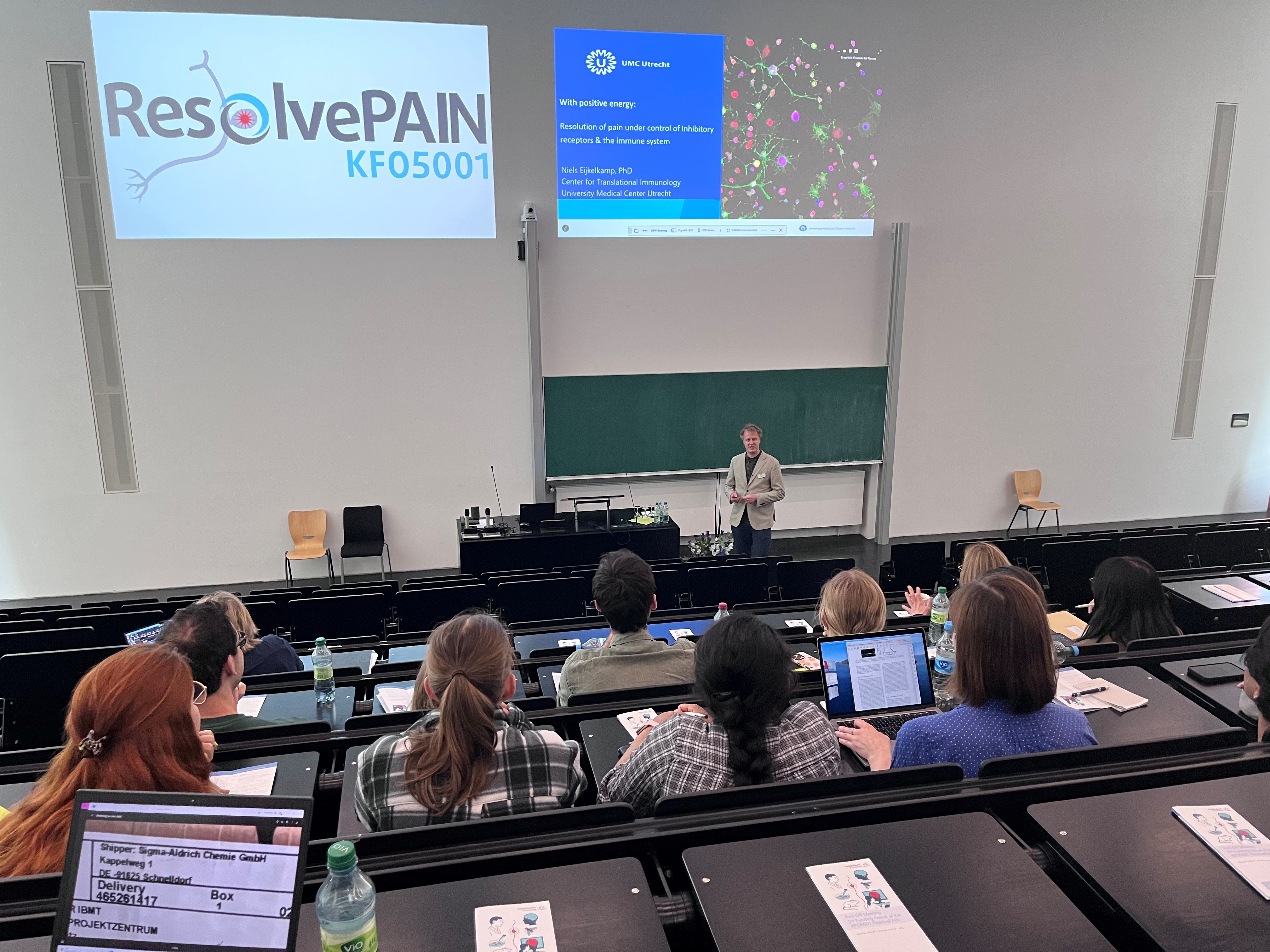 Prof. Dr. Niels Eijkelkamp im Hörsaal vor Gästen des Kick-Off-Meetings. An der Wand eine Powerpoint Präsentation und das Logo der Klinischen Forschungsgruppe KFO5001.