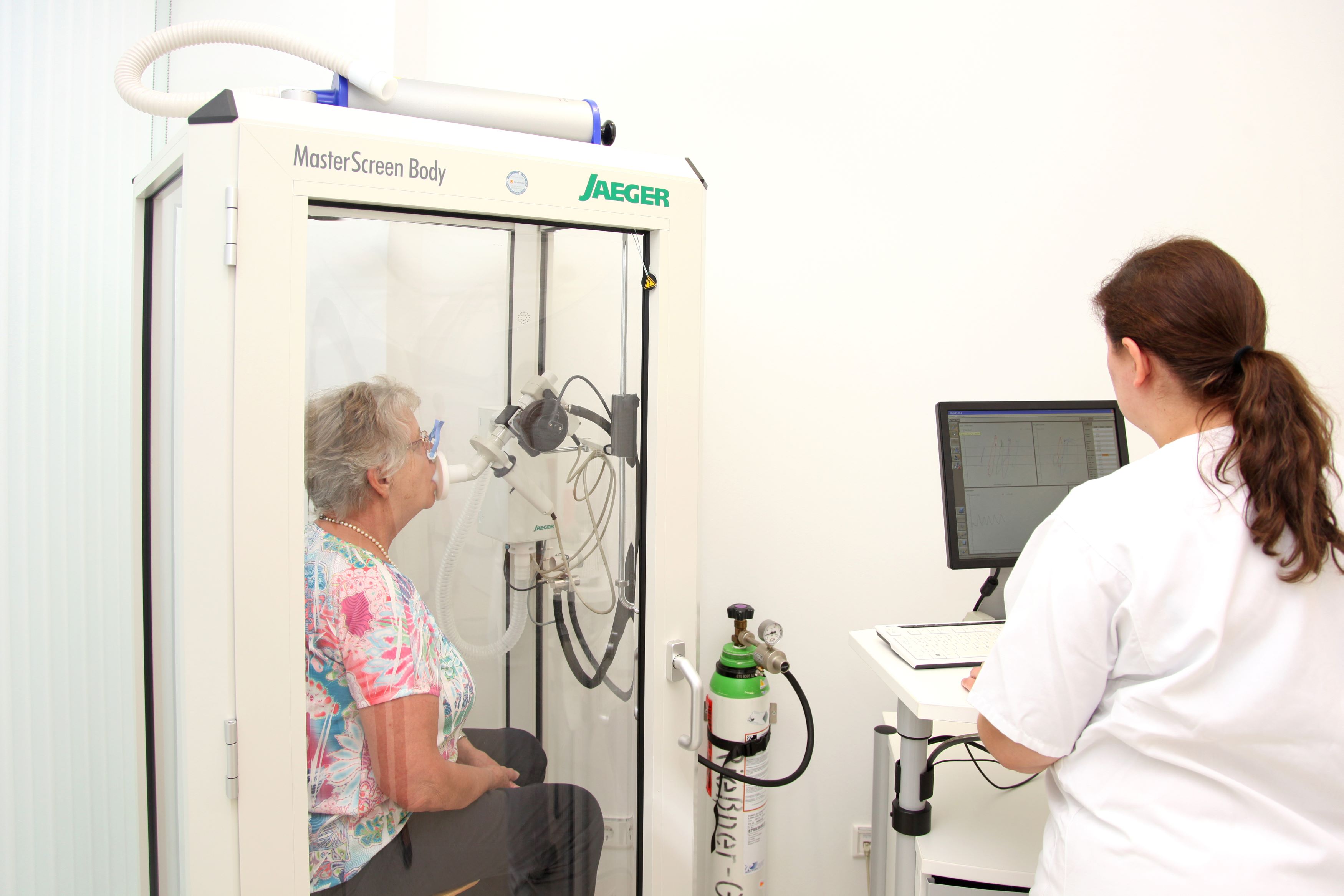Lungenfunktionstest Eine Patientin sitzt in einer Kabine mit Maske vor dem Mund, eine Nurse leitet sie an, kräftig auszuatmen.n.