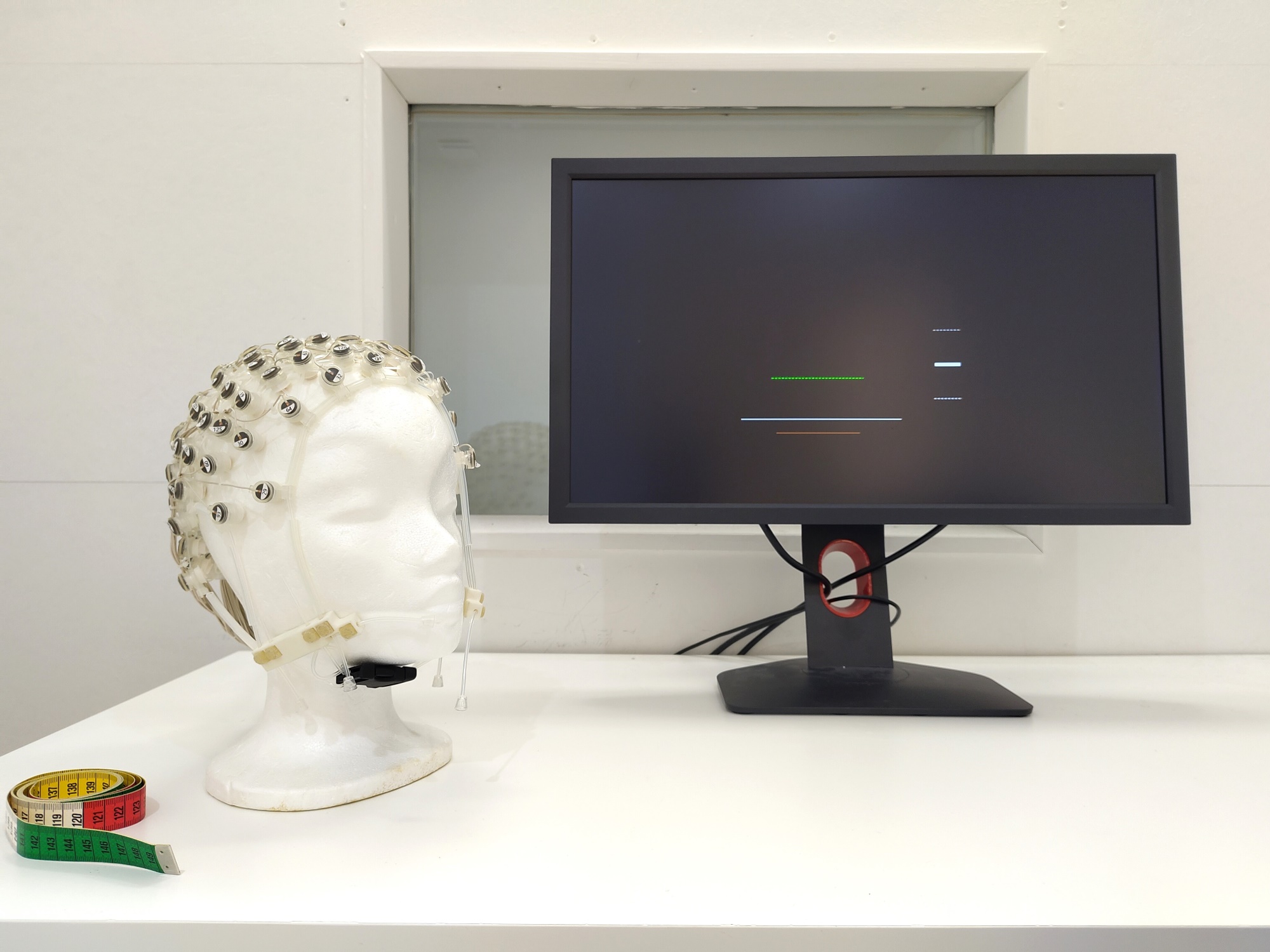 Bild vom Monitor, davor ist ein Kopfmodel mit EEG-Haube und ein Maßband 