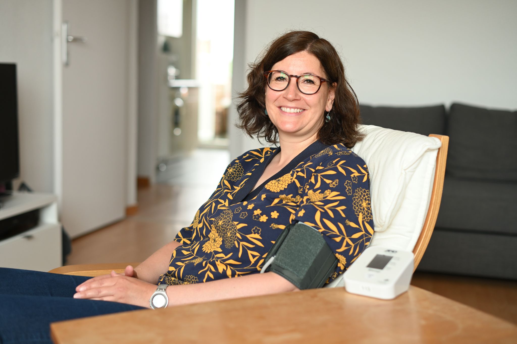 Telemedizin Patientin, die daheim am Wohnzimmertisch sitzt, misst ihren Blutdruck